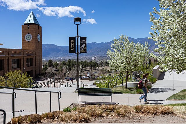 UCCS student walking on campus in the spring with the clock tower in the background
