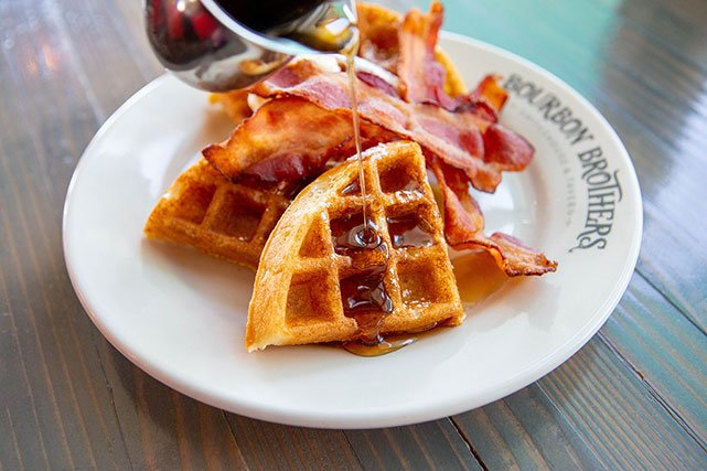 Bourbon Brothers waffles and bacon with syrup being poured